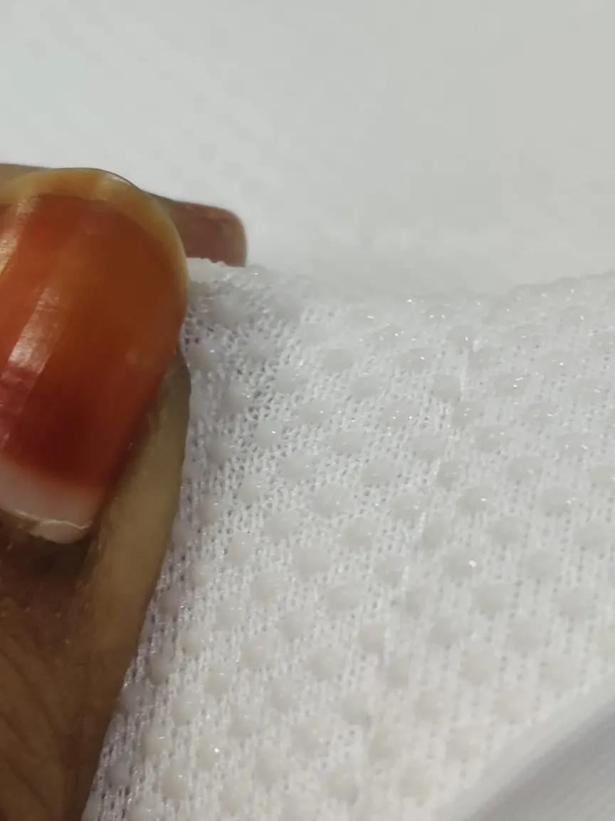 Close-up of white 2-ply fabric held between fingers, showing its raised dot pattern