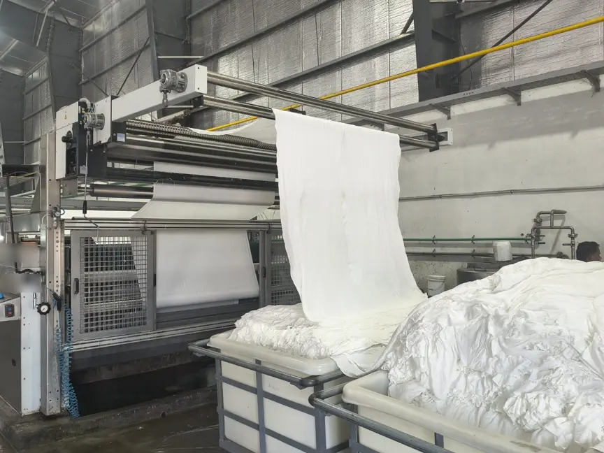 White fabric being drawn from collection trolleys up into a processing line