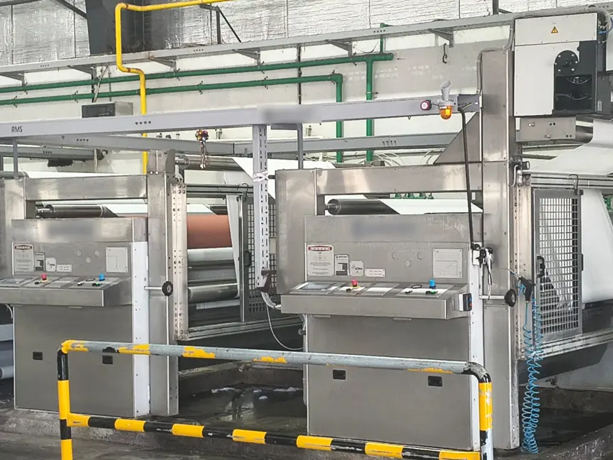 Fabric running through a finishing line, with two stainless-steel control stations in the foreground